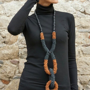 May include: A woman wearing a black turtleneck sweater and black pants with a long, brown and black necklace. She is wearing sunglasses and has her hair pulled back.