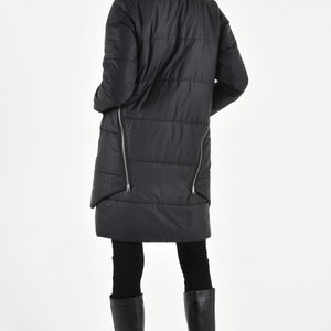 May include: A black quilted long coat with a high collar and zipper details on the sides. The coat is worn over black leggings and black knee-high boots.