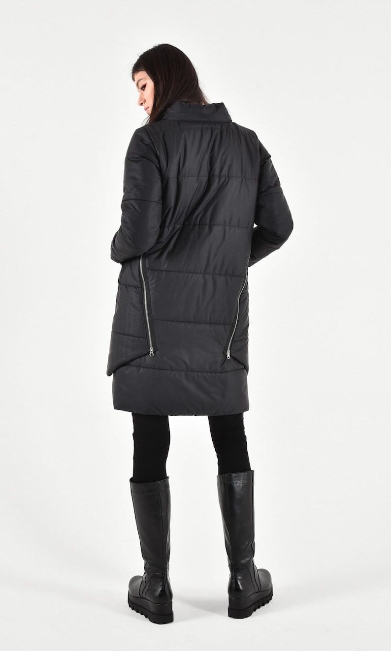 May include: A black quilted long coat with a high collar and zipper details on the sides. The coat is worn over black leggings and black knee-high boots.