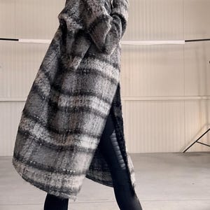 May include: A hooded, oversized coat in a gray and black plaid pattern. The coat is worn with black leggings and black ankle boots. The boots have a chunky sole. The coat appears to be made of a soft, textured fabric.