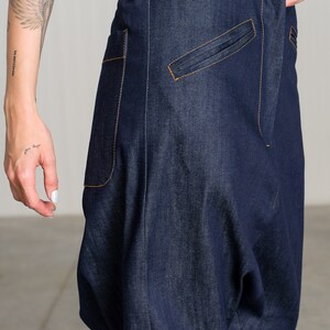 K&ouml;nnte beinhalten: Eine dunkelblaue Jeanshose mit einer einzigartigen, lockeren Passform. Die Hose hat einen einzigen Knopfverschluss und eine gro&szlig;e Tasche auf der rechten Seite.