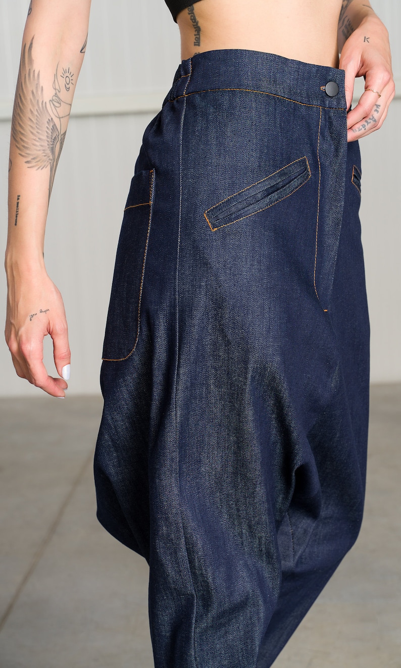 K&ouml;nnte beinhalten: Eine dunkelblaue Jeanshose mit einer einzigartigen, lockeren Passform. Die Hose hat einen einzigen Knopfverschluss und eine gro&szlig;e Tasche auf der rechten Seite.
