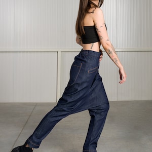K&ouml;nnte beinhalten: Eine Frau tr&auml;gt ein schwarzes Crop-Top und eine dunkelblaue Jeanshose mit einem einzigartigen, weiten Design. Sie tr&auml;gt schwarze Sneaker mit einer dicken Sohle.