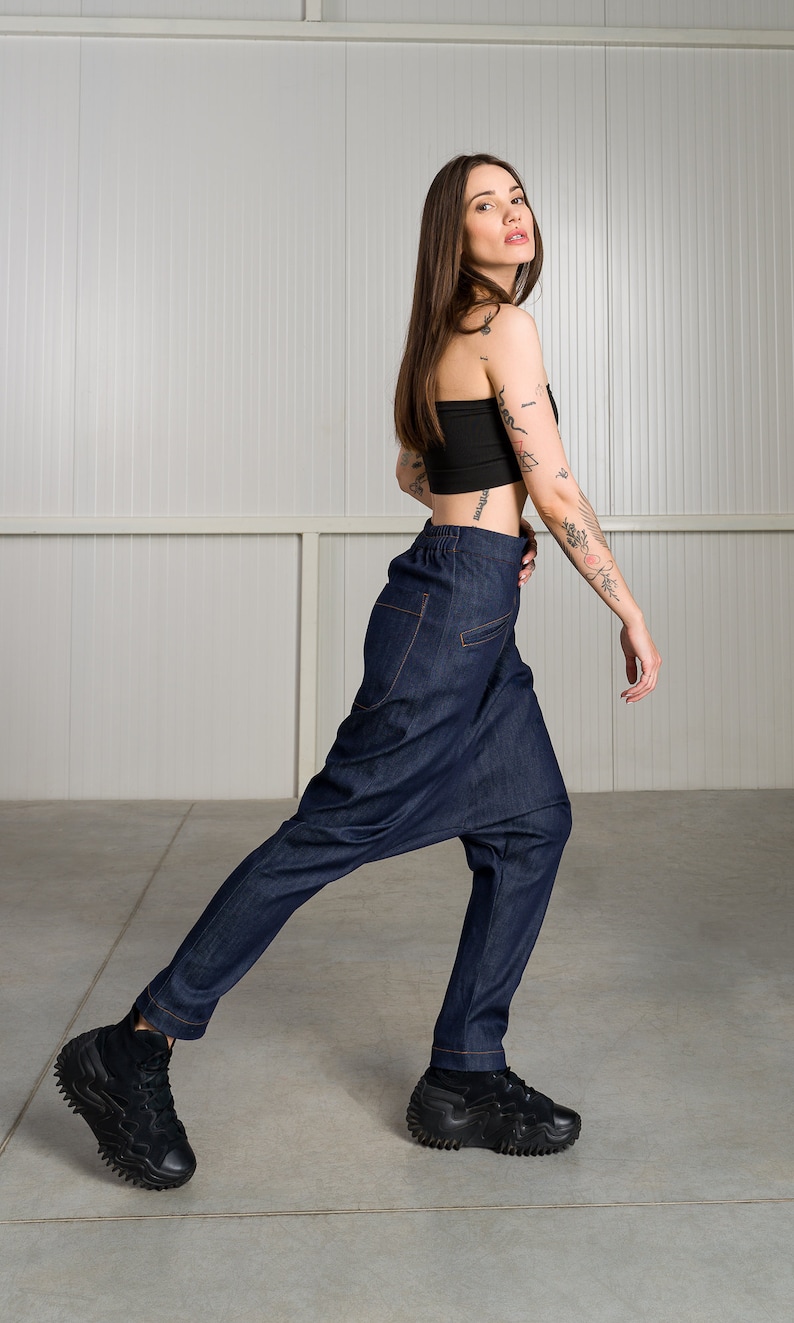 K&ouml;nnte beinhalten: Eine Frau tr&auml;gt ein schwarzes Crop-Top und eine dunkelblaue Jeanshose mit einem einzigartigen, weiten Design. Sie tr&auml;gt schwarze Sneaker mit einer dicken Sohle.