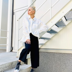 May include: A person wearing a white button-down shirt, black pants, and black high-top sneakers with a white sole and tan trim. The person is standing on concrete steps next to a metal staircase.