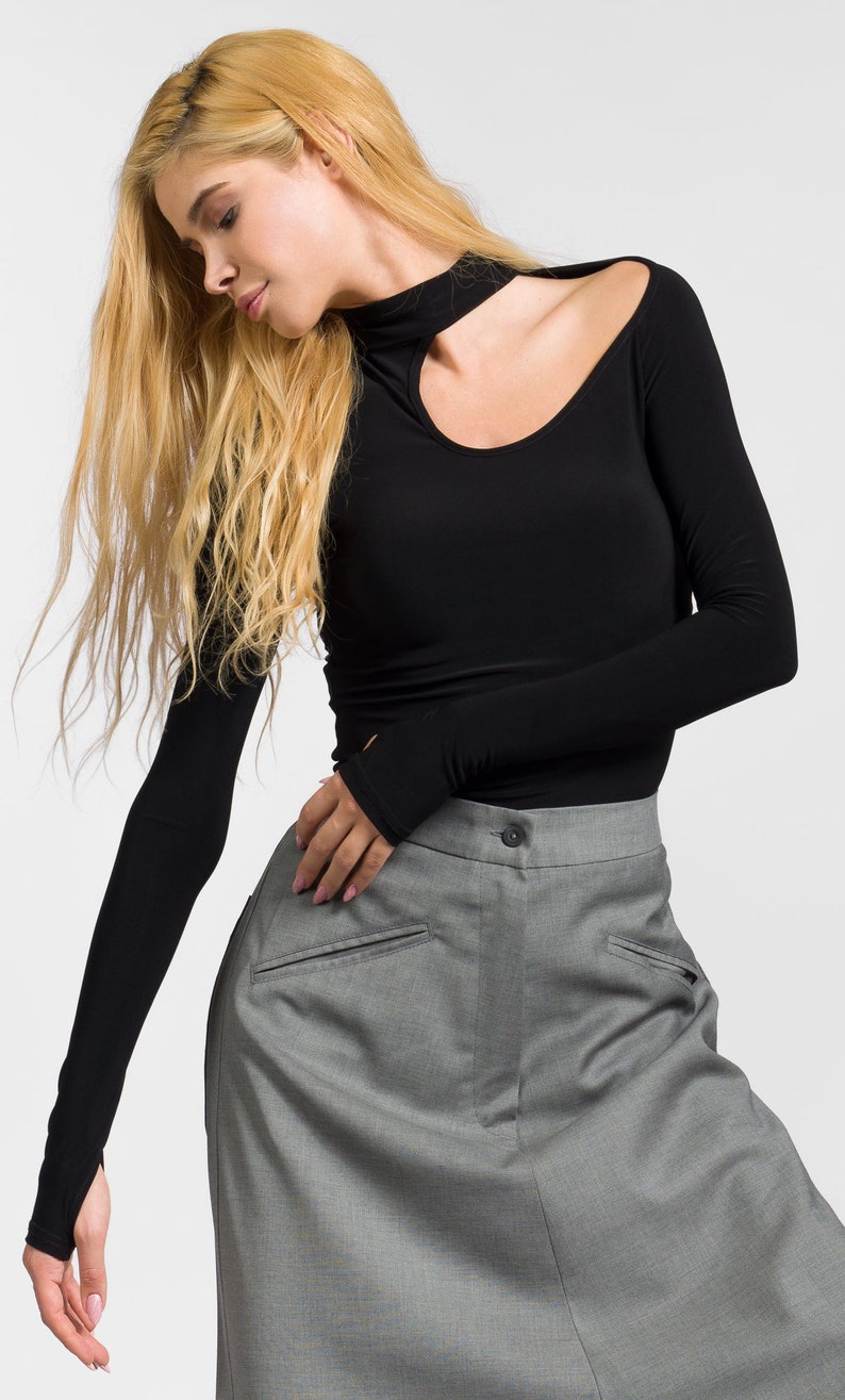 May include: A black long-sleeved shirt with a cutout neckline and thumbholes. The shirt is paired with a gray skirt.