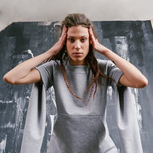 May include: A gray sweatshirt with long sleeves and a kangaroo pocket. The sleeves are extra long and have a wide, loose fit. The model is wearing the sweatshirt with pink pants.