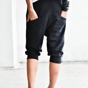 May include: Black cropped pants with a loose fit and cuffed hems. The pants have a unique design with a curved seam on the back.