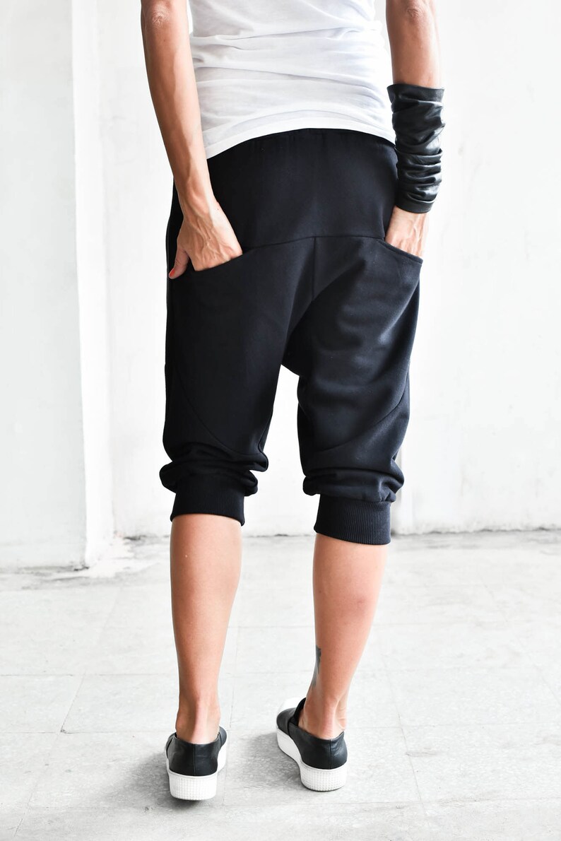 May include: Black cropped pants with a loose fit and cuffed hems. The pants have a unique design with a curved seam on the back.