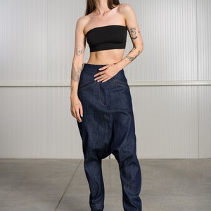K&ouml;nnte beinhalten: Eine Frau tr&auml;gt ein schwarzes Bandeau-Top und eine dunkelblaue Jeanshose mit weitem, lockerem Schnitt. Sie steht auf einem Betonboden vor einer wei&szlig;en Wand.