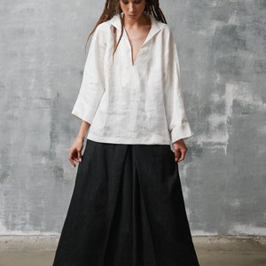 May include: A woman wearing a white linen shirt with a v-neck and a black linen skirt. She is wearing black and white high-top sneakers.