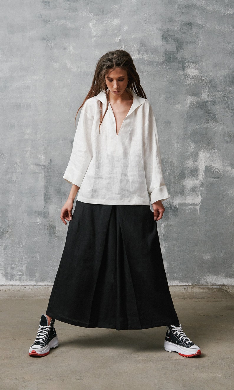 May include: A woman wearing a white linen shirt with a v-neck and a black linen skirt. She is wearing black and white high-top sneakers.