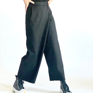 May include: A black wrap-style pant with a wide leg and a high waist. The pants are made of a smooth, lightweight fabric. The model is wearing black sneakers with white soles.