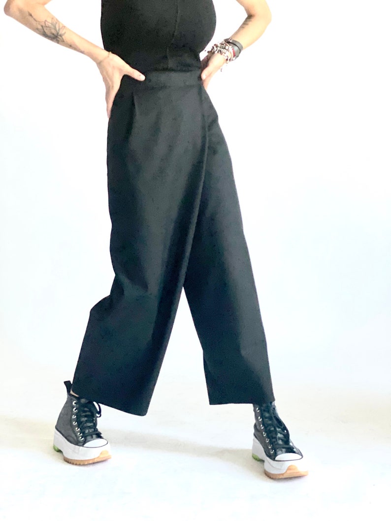 May include: A black wrap-style pant with a wide leg and a high waist. The pants are made of a smooth, lightweight fabric. The model is wearing black sneakers with white soles.