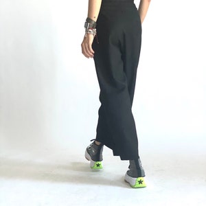 May include: A person wearing black pants and a black top with a pair of gray and white sneakers with a green accent.