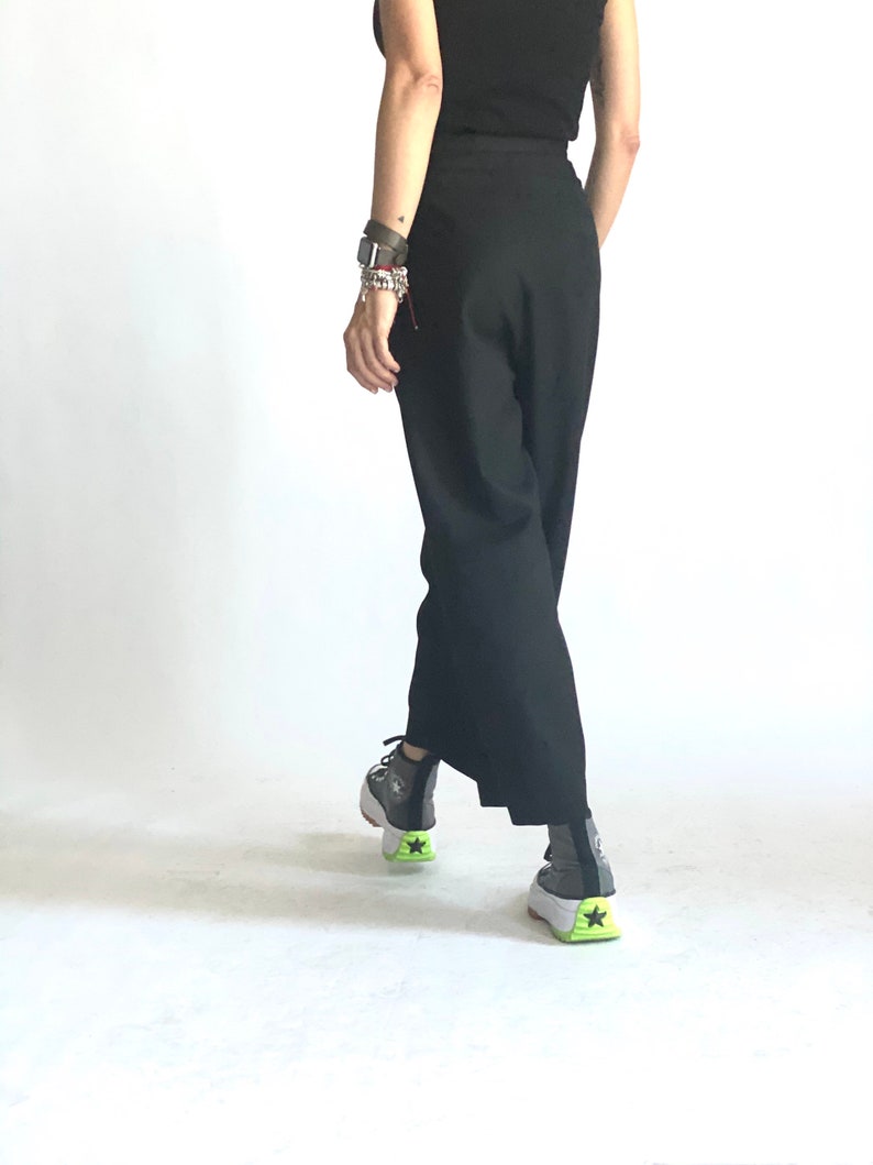 May include: A person wearing black pants and a black top with a pair of gray and white sneakers with a green accent.