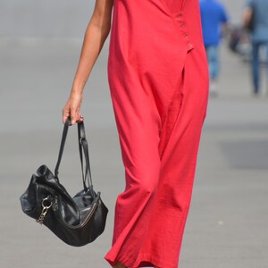 May include: A woman wearing a red sleeveless jumpsuit and black sandals carries a black leather handbag with a chain strap.