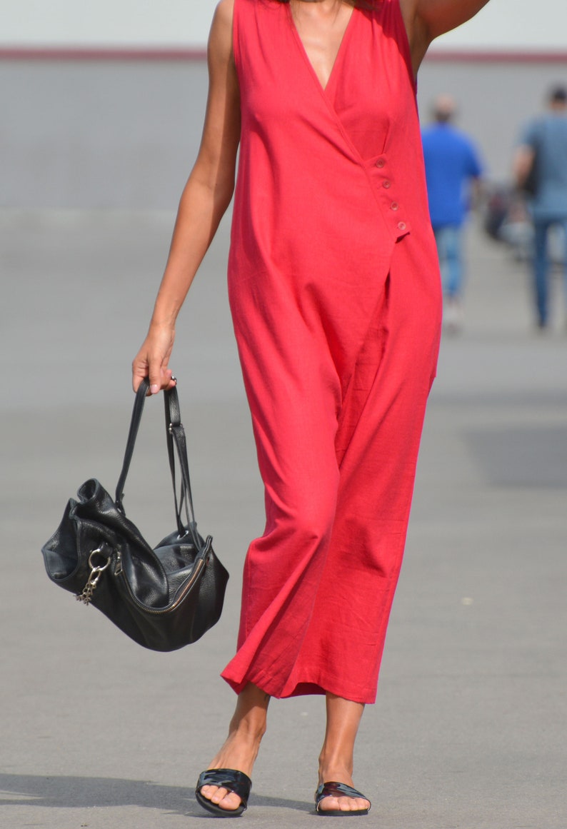 May include: A woman wearing a red sleeveless jumpsuit and black sandals carries a black leather handbag with a chain strap.