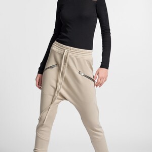 Puede incluir: Pantalones de ch&aacute;ndal beige con cintura el&aacute;stica y bolsillos con cremallera. Los pantalones tienen un corte holgado y un tiro bajo.