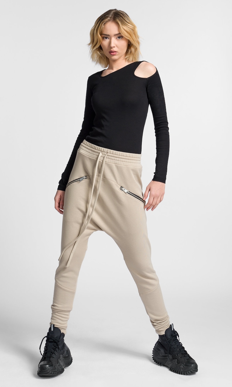 Puede incluir: Pantalones de ch&aacute;ndal beige con cintura el&aacute;stica y bolsillos con cremallera. Los pantalones tienen un corte holgado y un tiro bajo.