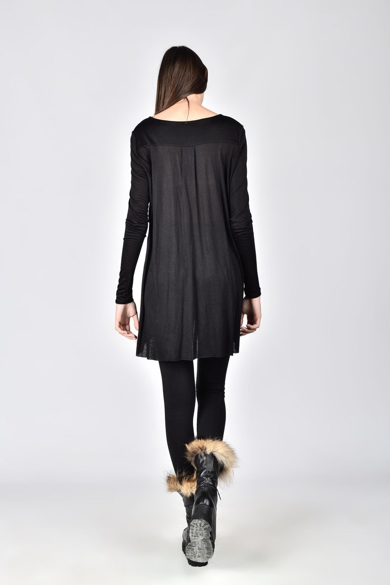 Op de afbeelding: Een zwarte tuniek met lange mouwen, een ronde hals en een vloeiend silhouet. Het model draagt ook een zwarte legging en zwarte laarzen met bont. De outfit staat tegen een effen witte achtergrond.