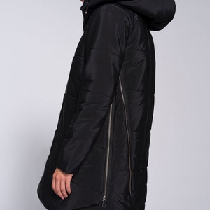May include: A black long puffer jacket with a hood and a zipper down the side. The jacket has a quilted design and a slightly asymmetrical hem.