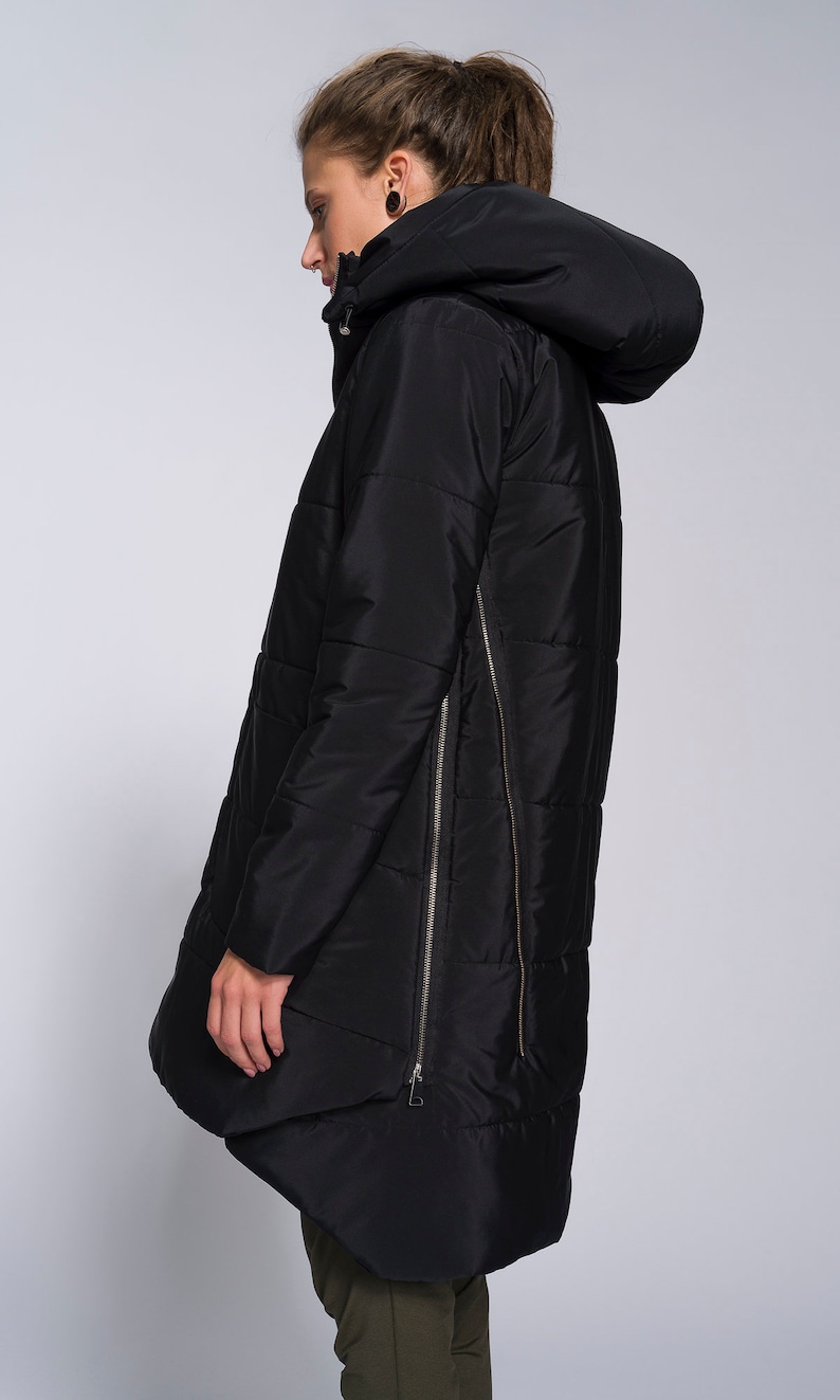 May include: A black long puffer jacket with a hood and a zipper down the side. The jacket has a quilted design and a slightly asymmetrical hem.