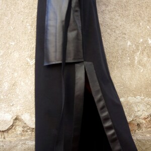 K&ouml;nnte beinhalten: Ein schwarzes Maxikleid mit einem Lederpanel und einem seitlichen Schlitz. Das Kleid wird mit schwarzen Schn&uuml;rschuhen mit einem burgunderfarbenen Akzent kombiniert.