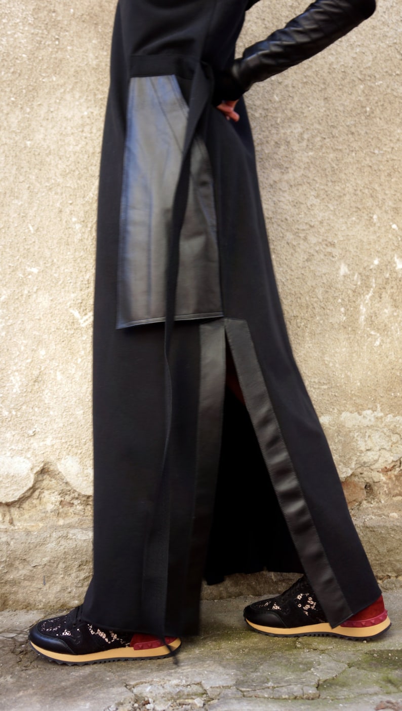 K&ouml;nnte beinhalten: Ein schwarzes Maxikleid mit einem Lederpanel und einem seitlichen Schlitz. Das Kleid wird mit schwarzen Schn&uuml;rschuhen mit einem burgunderfarbenen Akzent kombiniert.