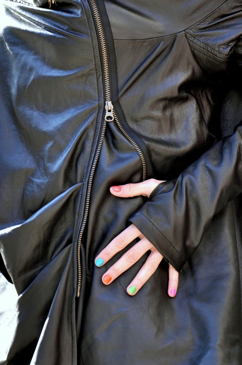 May include: A black leather jacket with a zipper closure. The jacket is unzipped and the person's hand is visible with colorful nail polish.