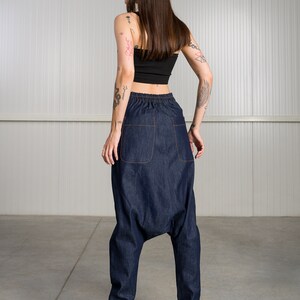 K&ouml;nnte beinhalten: Eine Person tr&auml;gt ein schwarzes Crop-Top und eine dunkelblaue Jeanshose mit weitem, lockerem Sitz. Die Hose hat einen Kordelzugbund und ist an den Kn&ouml;cheln umgeschlagen. Die Person tr&auml;gt schwarze Turnschuhe.