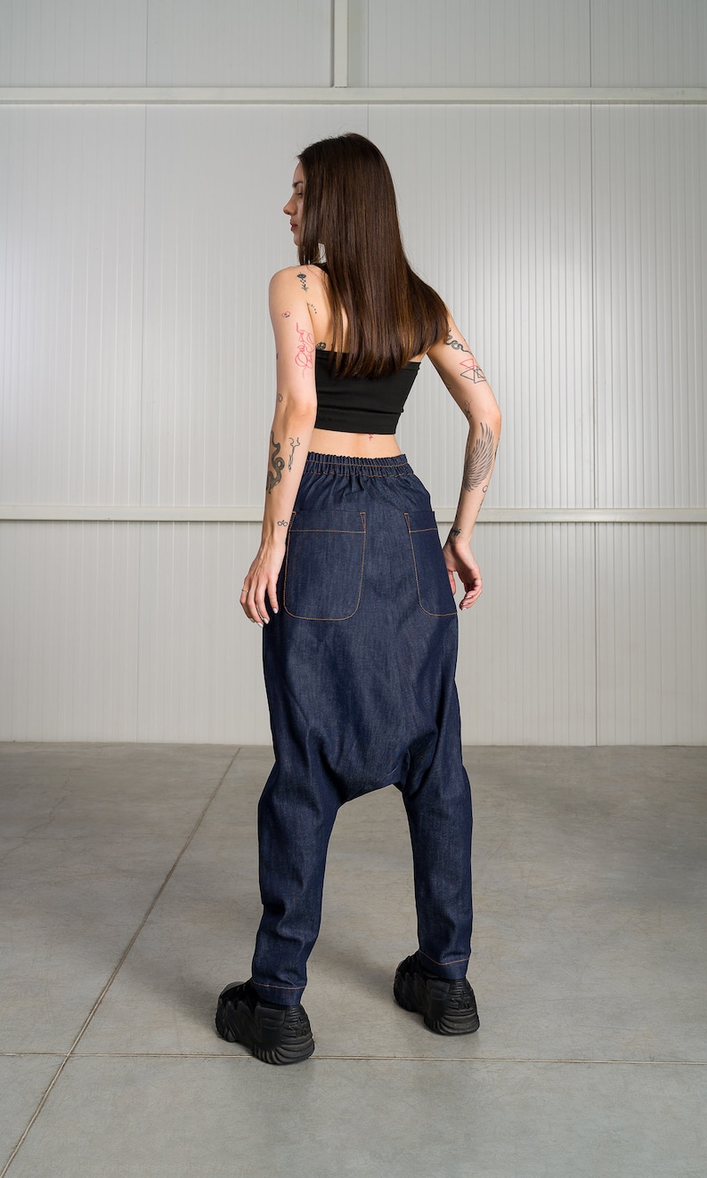 K&ouml;nnte beinhalten: Eine Person tr&auml;gt ein schwarzes Crop-Top und eine dunkelblaue Jeanshose mit weitem, lockerem Sitz. Die Hose hat einen Kordelzugbund und ist an den Kn&ouml;cheln umgeschlagen. Die Person tr&auml;gt schwarze Turnschuhe.