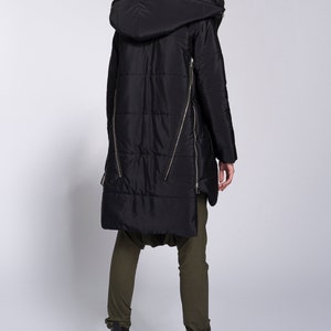May include: Black long puffer jacket with a hood and zipper details. The jacket has a quilted design and is worn with olive green pants and black boots.