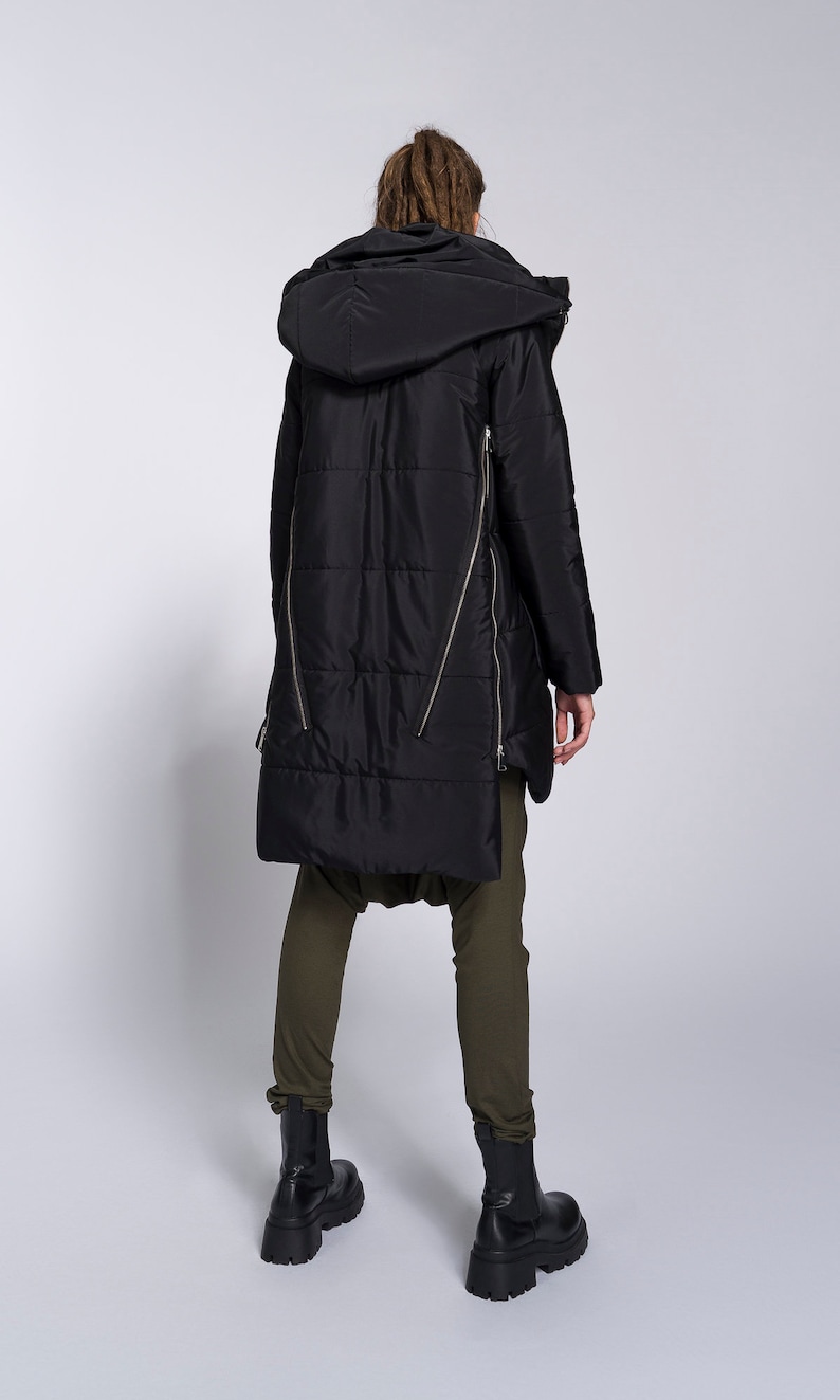 May include: Black long puffer jacket with a hood and zipper details. The jacket has a quilted design and is worn with olive green pants and black boots.