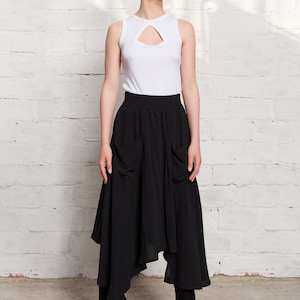 Pode incluir: Uma mulher vestindo um top branco sem mangas com um decote de chave e uma saia preta assim&eacute;trica com bolsos. Ela est&aacute; usando t&ecirc;nis preto e branco com detalhes vermelhos.