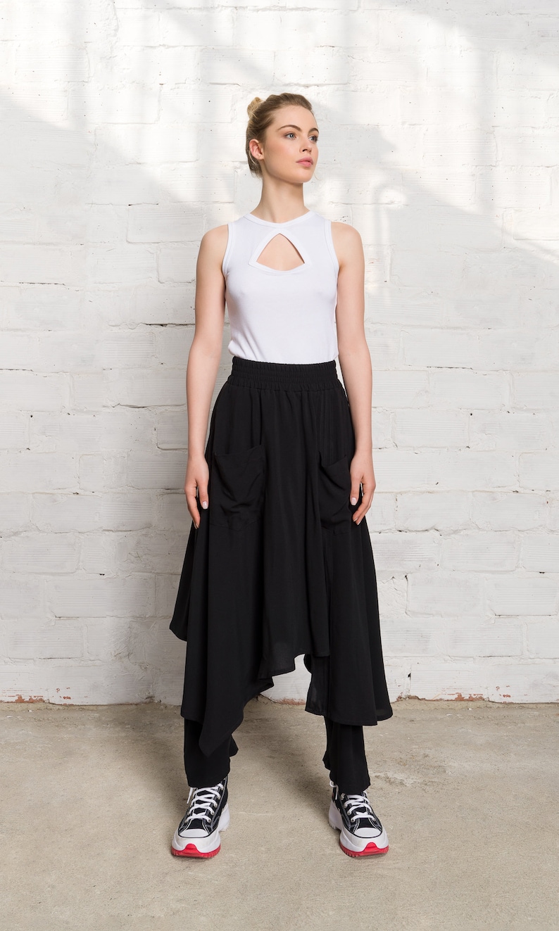 Pode incluir: Uma mulher vestindo um top branco sem mangas com um decote de chave e uma saia preta assim&eacute;trica com bolsos. Ela est&aacute; usando t&ecirc;nis preto e branco com detalhes vermelhos.
