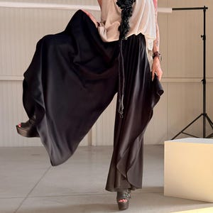 Puede incluir: Pantalones palazzo negros de pernera ancha con un diseño fluido. Los pantalones se combinan con un top color crema y tacones de plataforma. Un collar floral negro añade un contraste llamativo al conjunto. El conjunto es adecuado para diversas ocasiones.