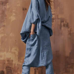 May include: A blue linen jumpsuit with a loose-fitting top and wide-leg pants. The jumpsuit has a relaxed, comfortable fit and features a drawstring waist. The model is wearing white sneakers with green accents.