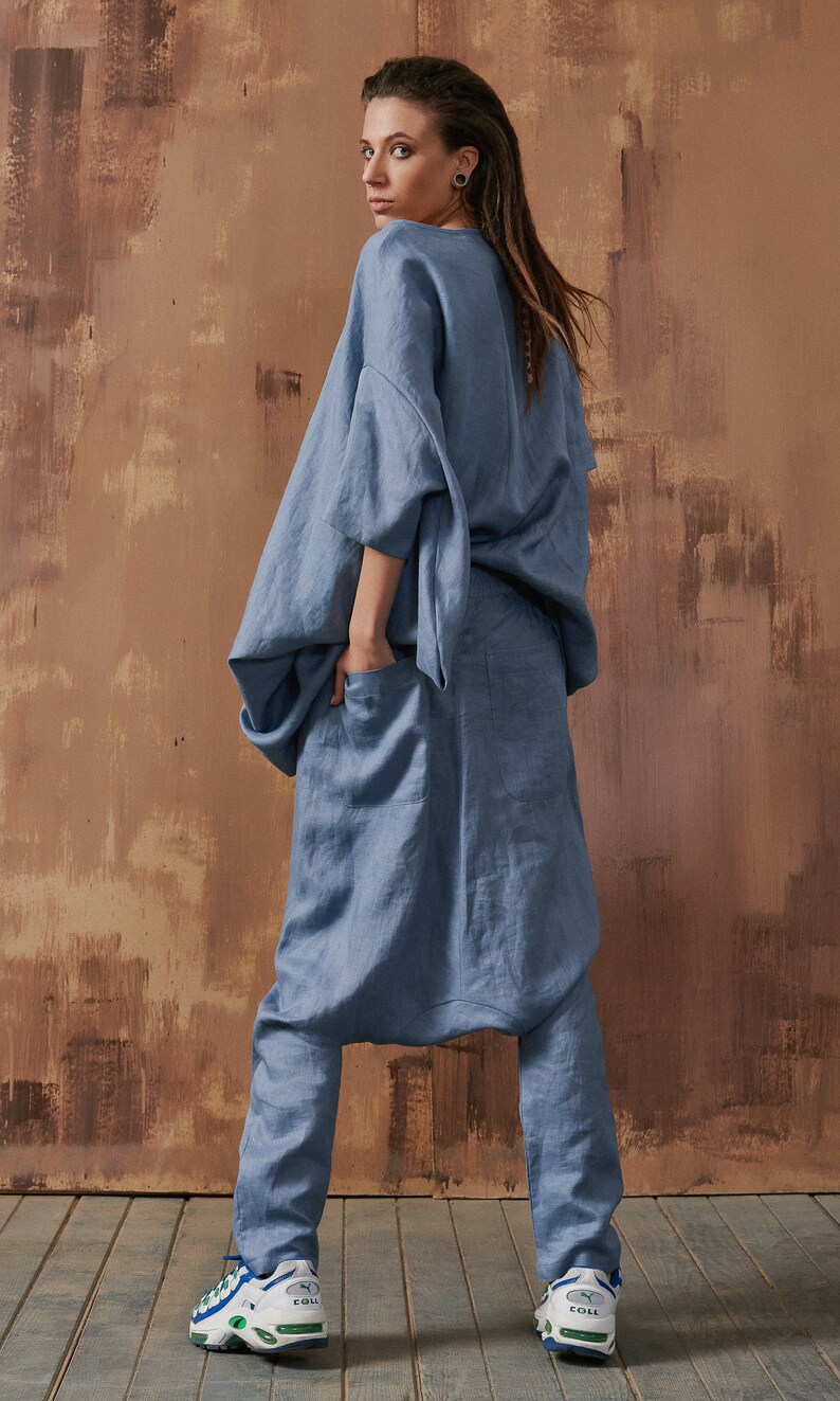May include: A blue linen jumpsuit with a loose-fitting top and wide-leg pants. The jumpsuit has a relaxed, comfortable fit and features a drawstring waist. The model is wearing white sneakers with green accents.