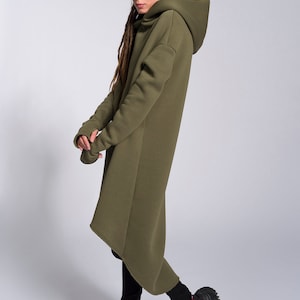 May include: A long, olive green hooded sweatshirt with a high neckline and a slightly asymmetrical hem. The sweatshirt is made of a soft, comfortable fabric and has a relaxed fit.