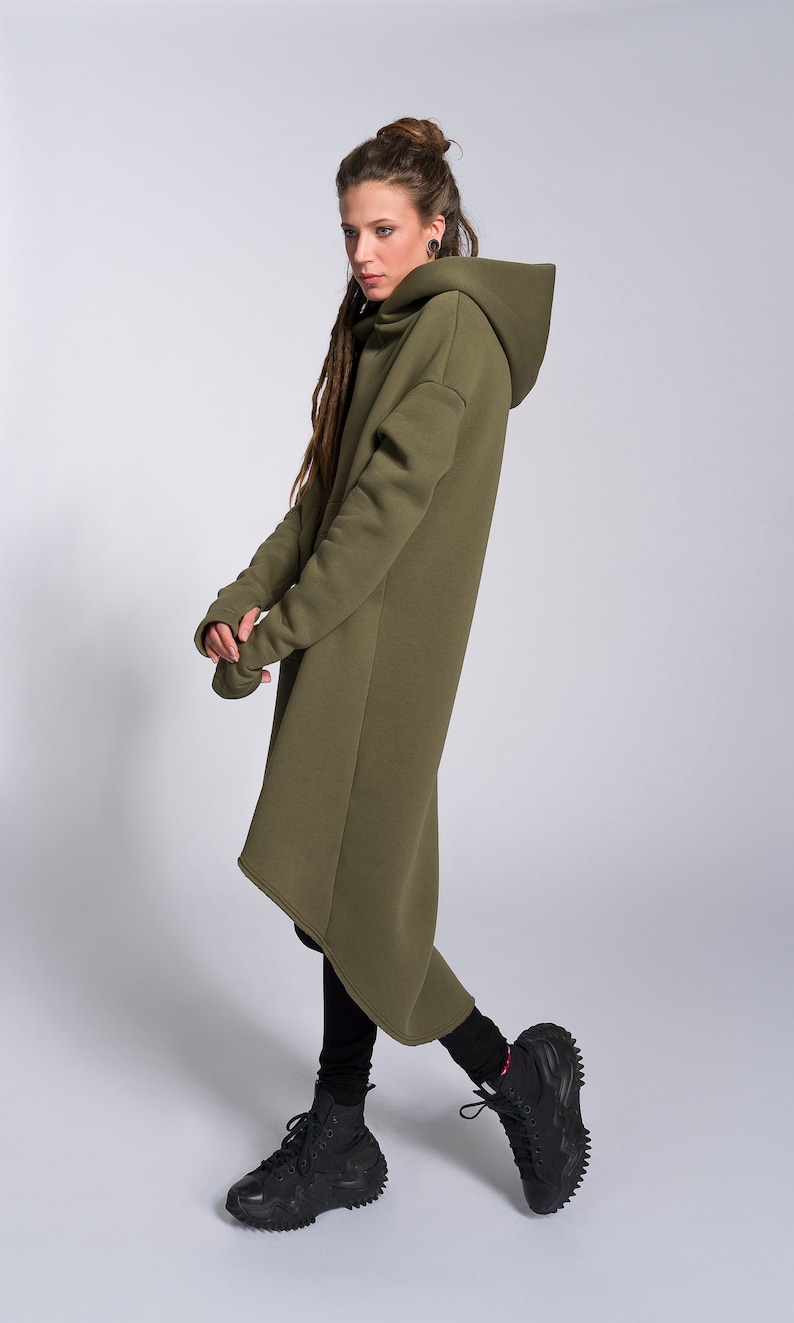 May include: A long, olive green hooded sweatshirt with a high neckline and a slightly asymmetrical hem. The sweatshirt is made of a soft, comfortable fabric and has a relaxed fit.
