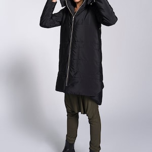 May include: A black long puffer jacket with a hood. The jacket has a zipper closure and a quilted design. The model is wearing the jacket with the hood pulled up over their head.
