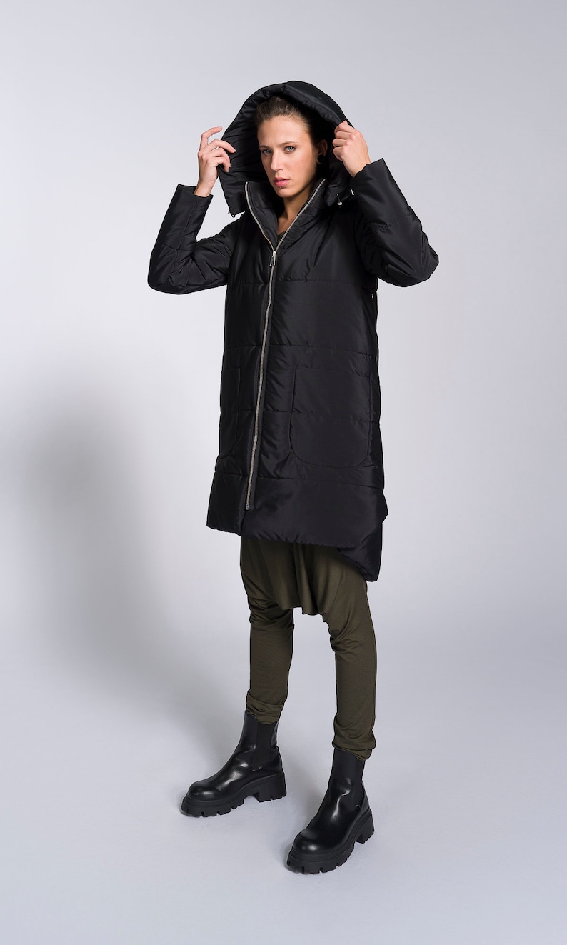 May include: A black long puffer jacket with a hood. The jacket has a zipper closure and a quilted design. The model is wearing the jacket with the hood pulled up over their head.