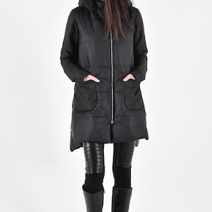 May include: A black long puffer jacket with a hood and zipper closure. The jacket has a quilted design and large pockets. The model is wearing black leggings and tall black boots.