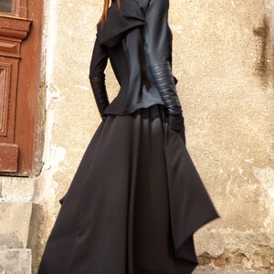 May include: A black hooded jacket with a long, flowing skirt. The jacket has leather accents on the sleeves and the skirt has a unique asymmetrical design. The person is wearing black sneakers with white laces.