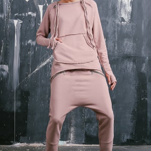 Peut inclure: Une femme portant un sweat-shirt rose et un pantalon assorti avec un aspect d&eacute;lav&eacute;. Le sweat-shirt a une grande poche et le pantalon a deux poches zipp&eacute;es. Elle porte des baskets.