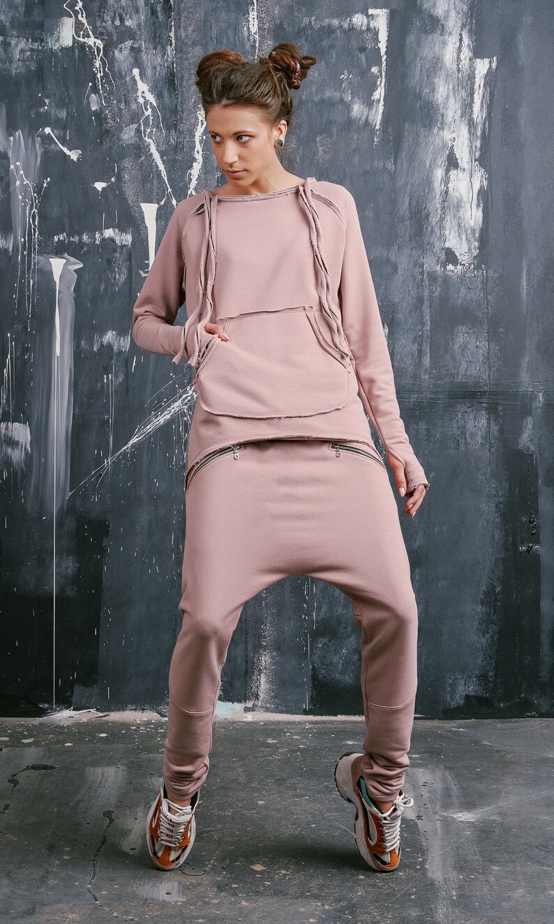 Peut inclure: Une femme portant un sweat-shirt rose et un pantalon assorti avec un aspect d&eacute;lav&eacute;. Le sweat-shirt a une grande poche et le pantalon a deux poches zipp&eacute;es. Elle porte des baskets.