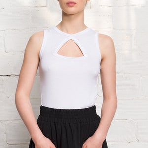 Pode incluir: Uma mulher vestindo um top branco sem mangas com um decote de chave e uma saia preta com bolsos.