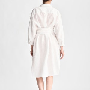 May include: A white linen shirt dress with a self-tie belt. The dress has a relaxed fit and a slightly A-line silhouette.