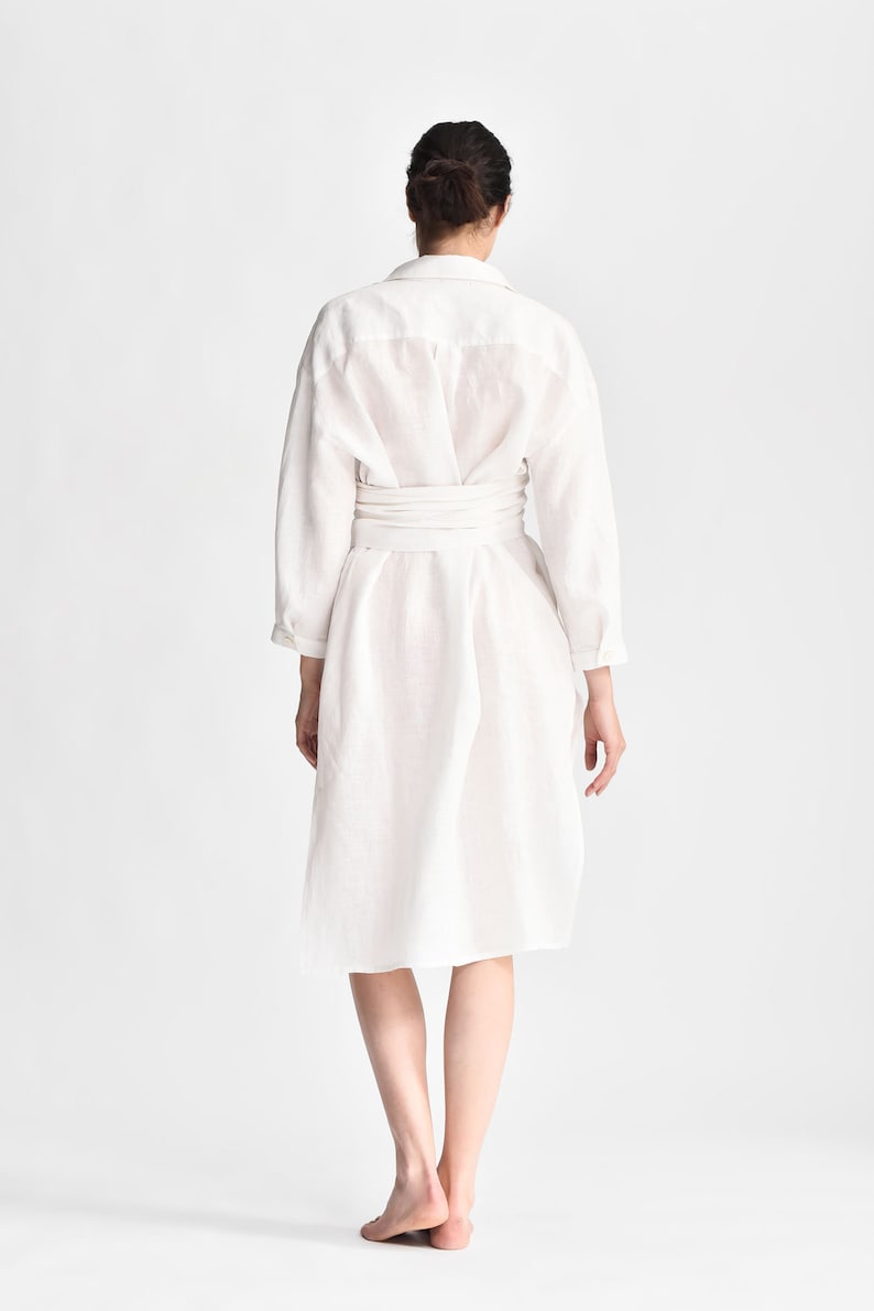 May include: A white linen shirt dress with a self-tie belt. The dress has a relaxed fit and a slightly A-line silhouette.